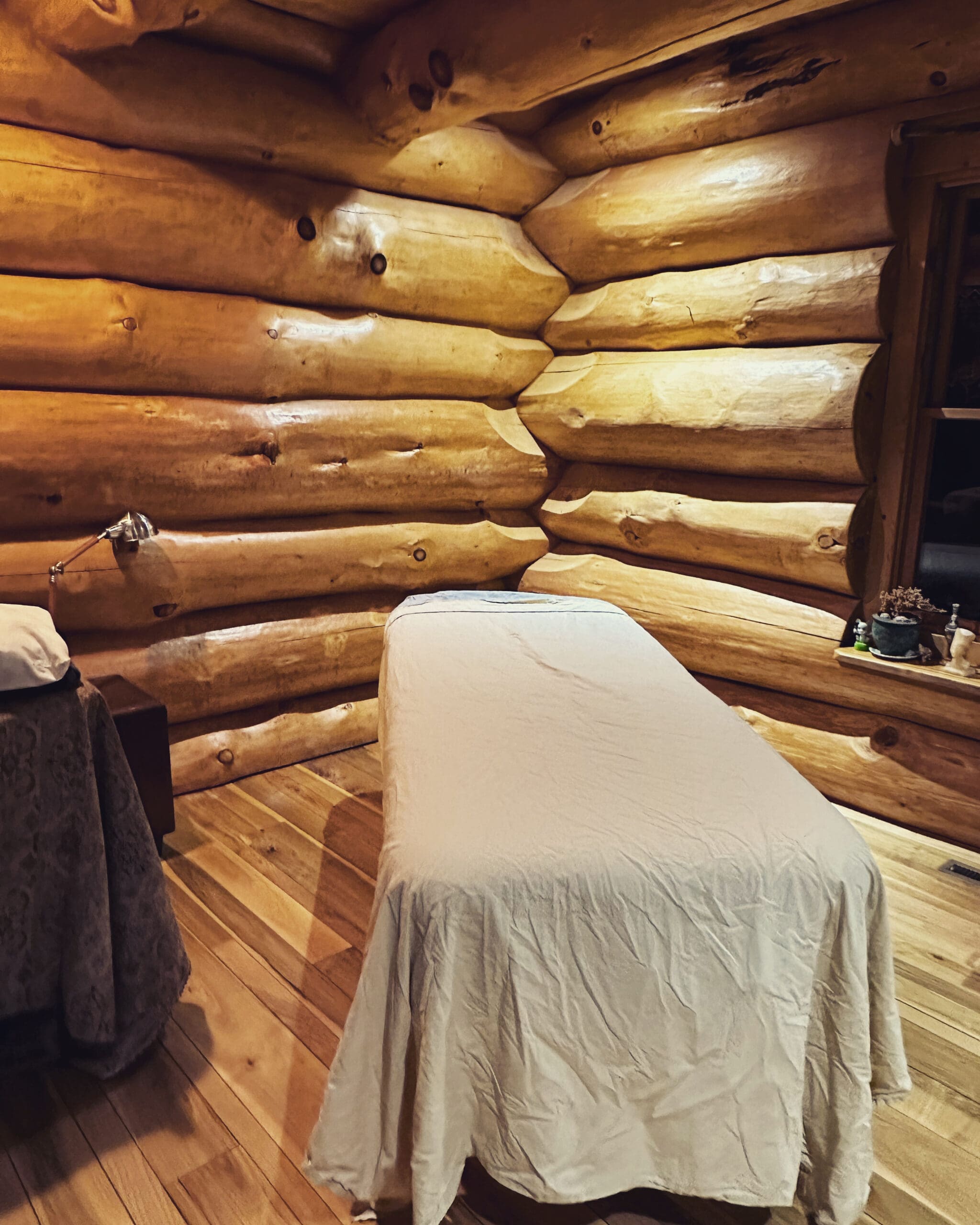 massage table with sheets on it in the corner of a room in a log cabin